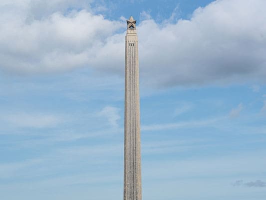 A tall, slender stone monument with a star at the top stands against a blue sky with scattered clouds.