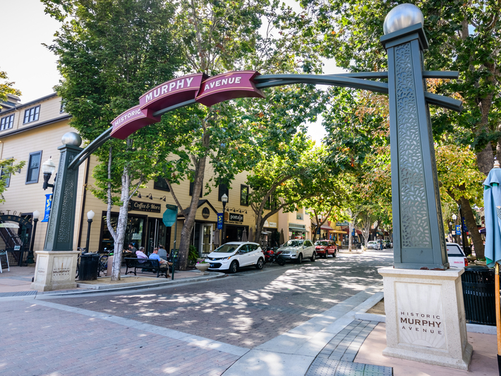 A decorative archway labeled Historic Murphy Avenue spans a tree-lined street with parked cars, pedestrians, and cafes on a sunny day.